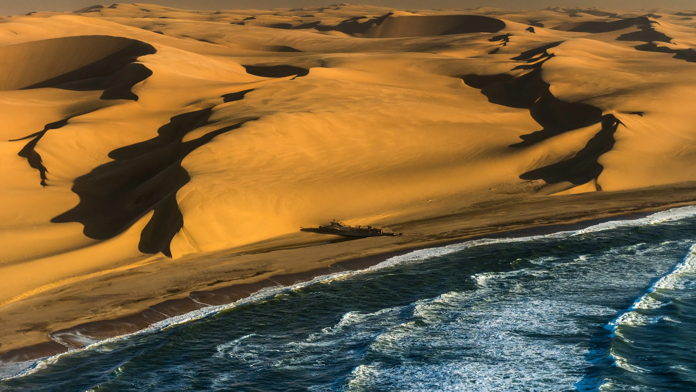 An aerial view of a shipwreck between Namib dunes and the Atlantic shoreline