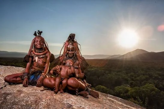 Two Himba women seated in a rocky Namibian landscape at sunset