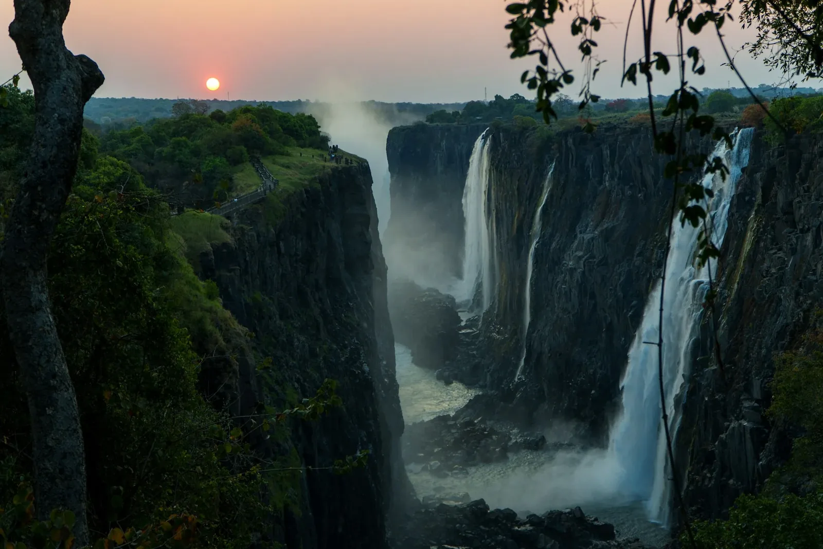 Victoria Falls in warm light with green foliage beside the gorge