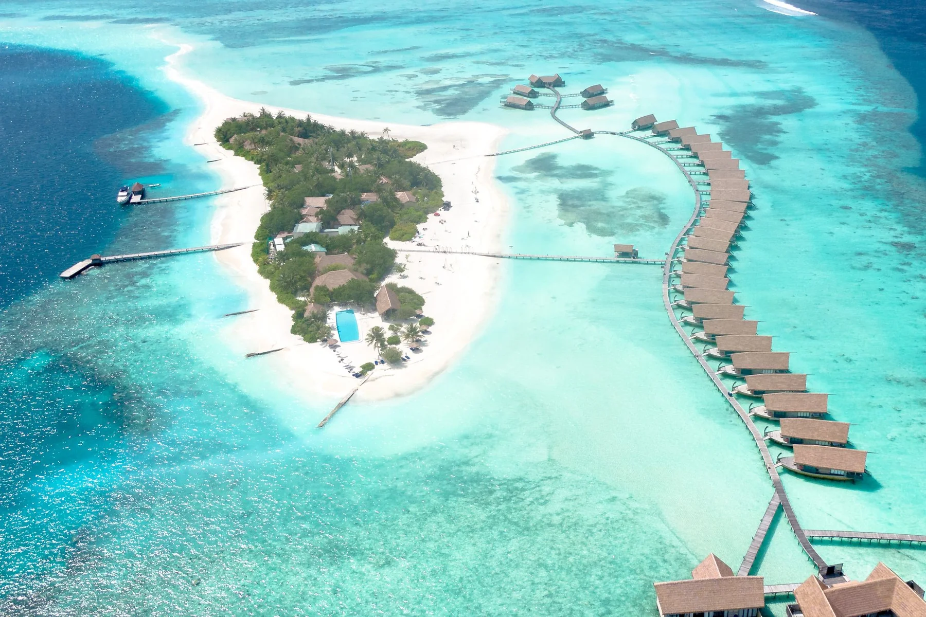 A white-sand Maldivian island and curved overwater villas surrounded by a turquoise lagoon